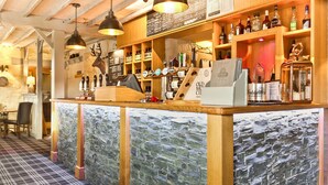 A bar area with a stone wall backdrop, wooden shelves with bottles, and a mounted deer head.