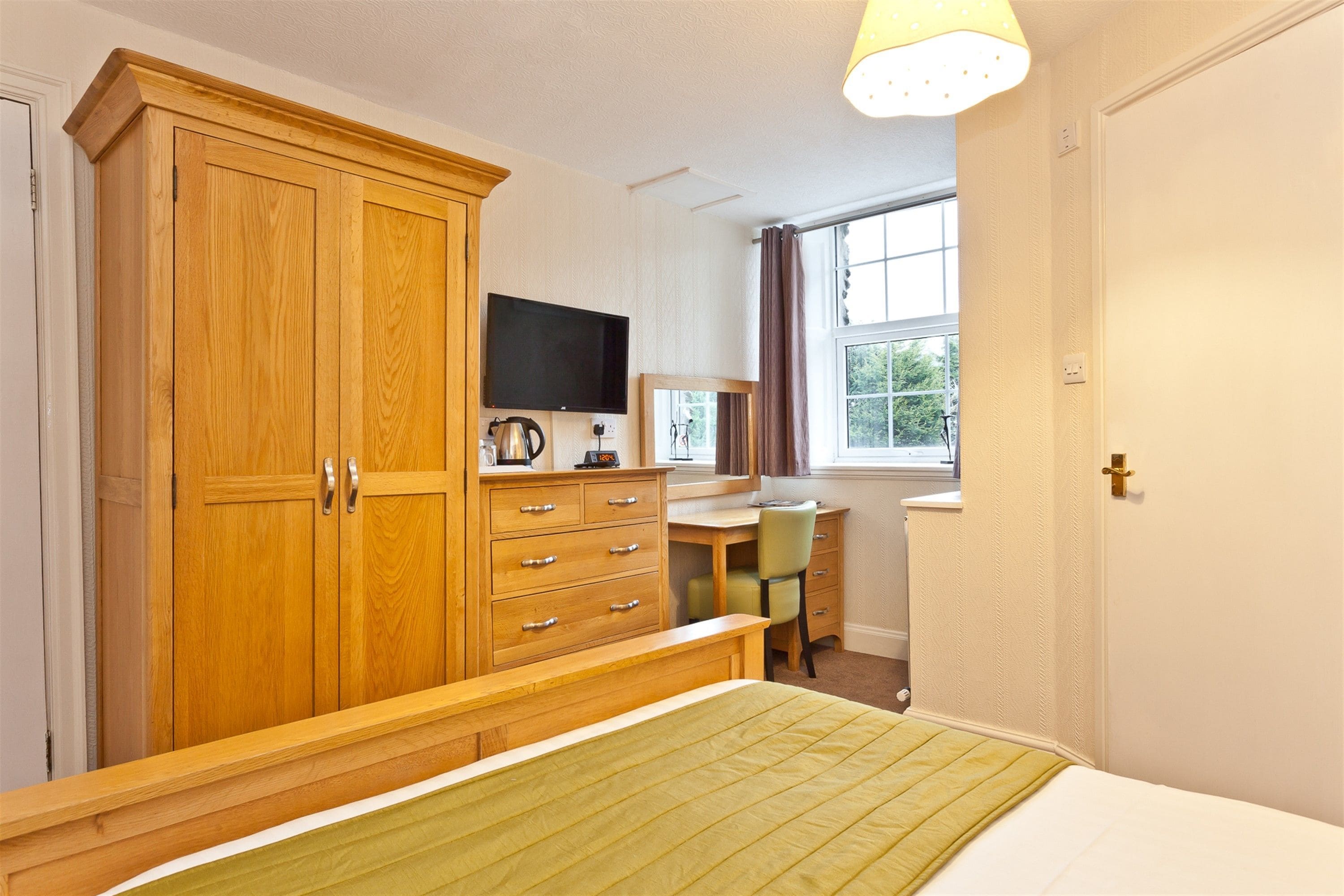 A bedroom with a bed, wooden wardrobe, desk, chair, and a television.