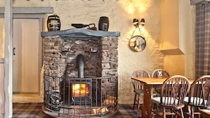 A stone fireplace with a log fire, surrounded by plaid-patterned flooring and wooden chairs.