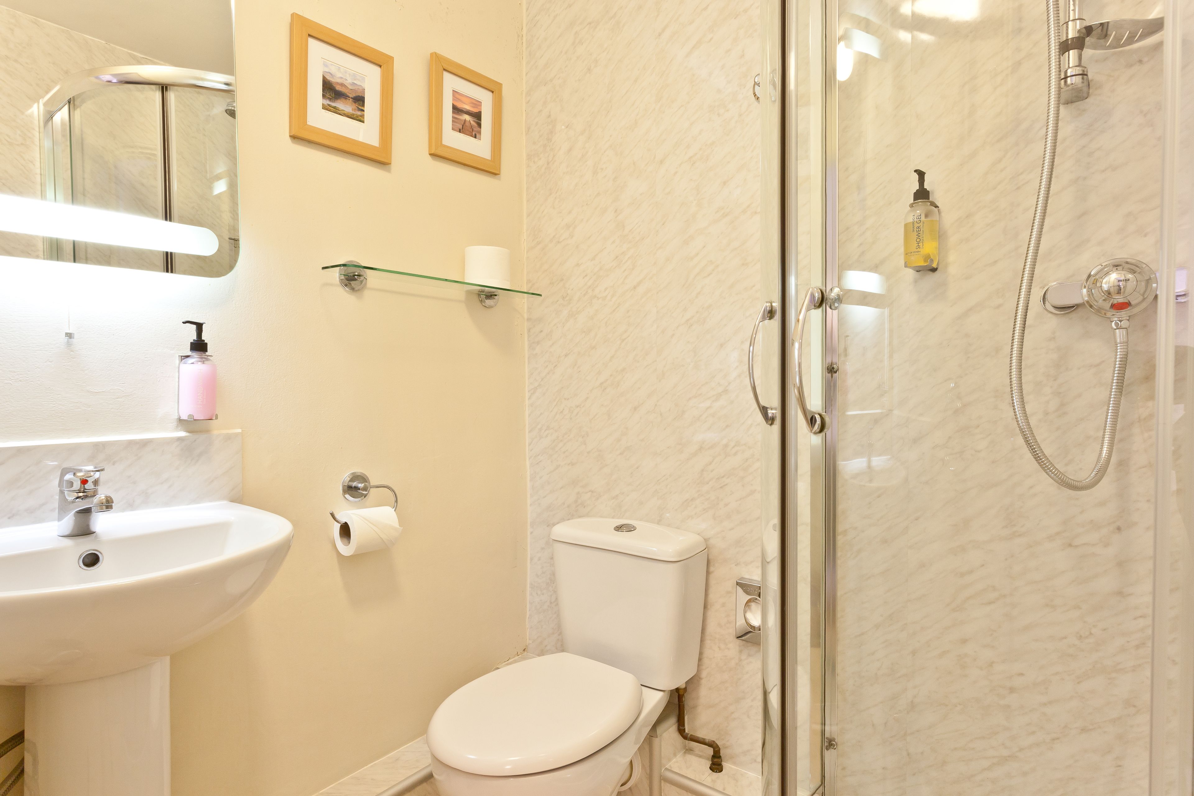 Une salle de bain avec un lavabo, des toilettes et une douche. Deux tableaux encadrés sont accrochés au mur.