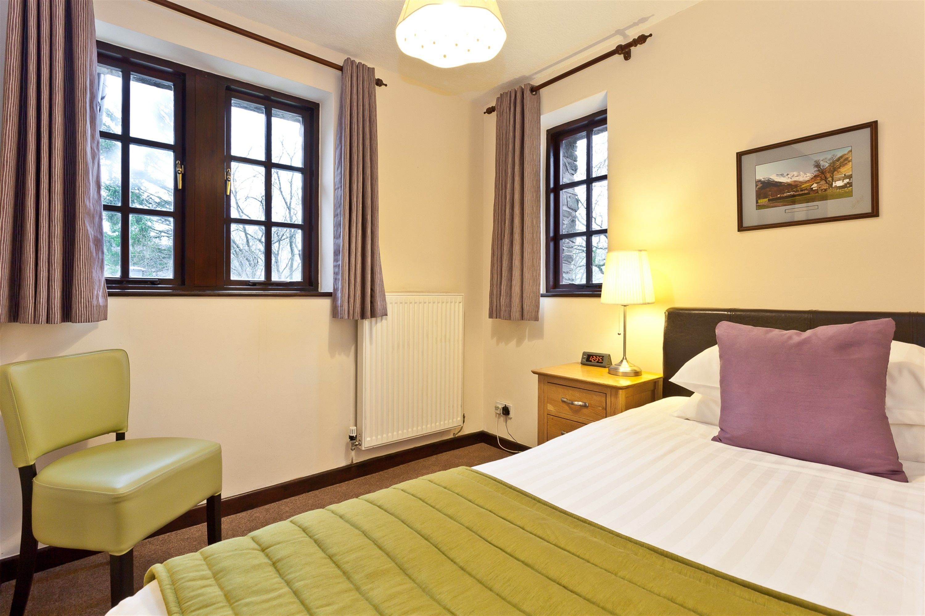 A hotel room with a bed, a chair, a nightstand, a lamp, and a picture on the wall.