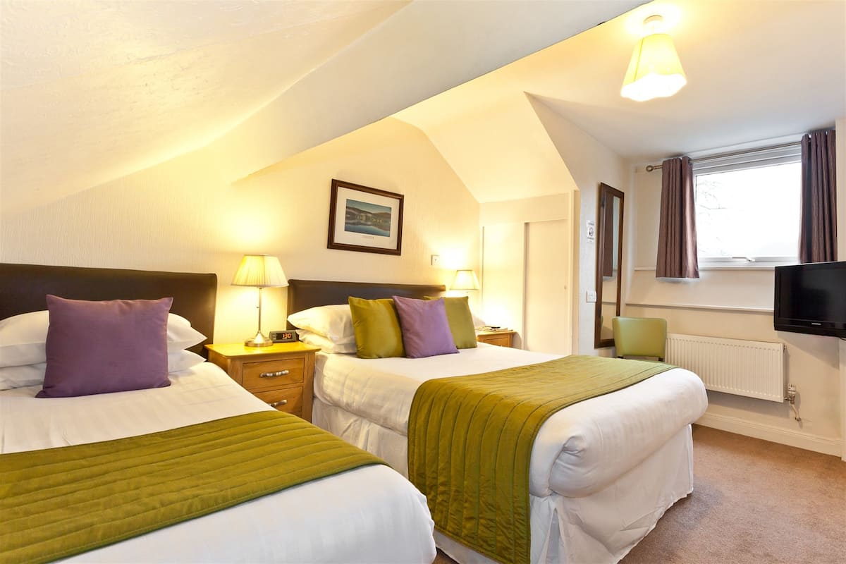 A hotel room with two beds, a television, a window with curtains, and a framed picture on the wall.