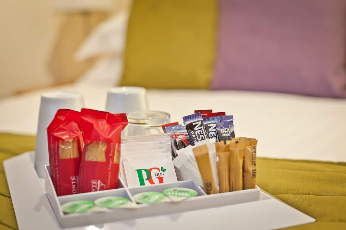 A tray with food items and a bottle on a bed with pillows.