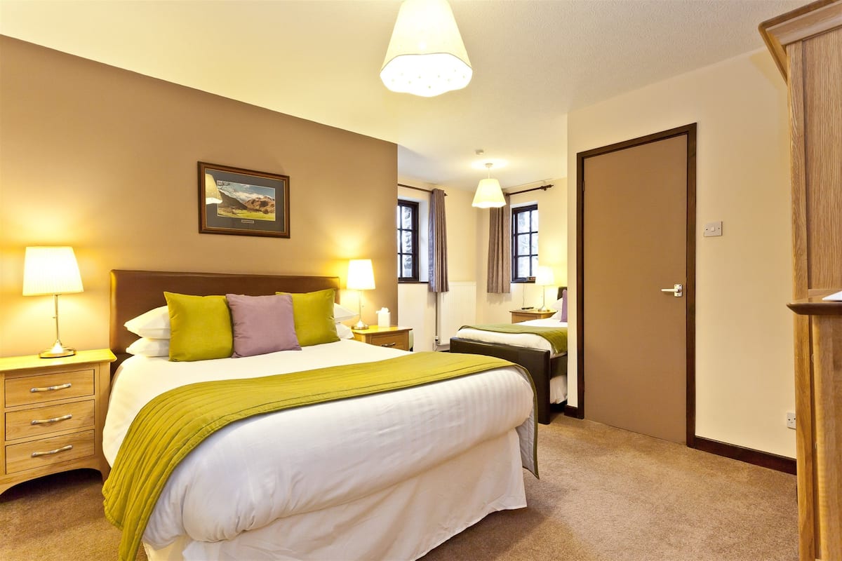 A hotel room with a large bed, two bedside tables with lamps, a wooden wardrobe, and a door.