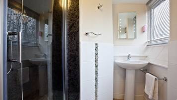 A modern bathroom with a glass-enclosed shower, a white pedestal sink, and a mirror with lights.