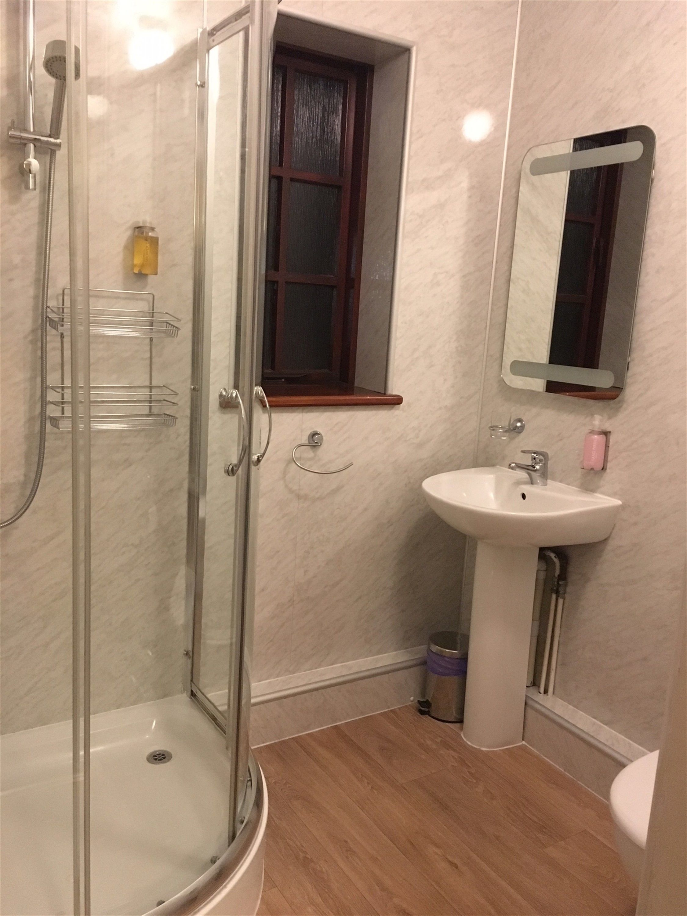 Un baño con ducha de mampara de vidrio, lavabo blanco y espejo sobre el lavabo.