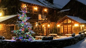 A rustic lodge with a snow-covered exterior, a Christmas tree with lights, and outdoor seating.