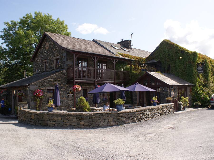 A stone building with a balcony, outdoor seating with umbrellas, and potted plants.