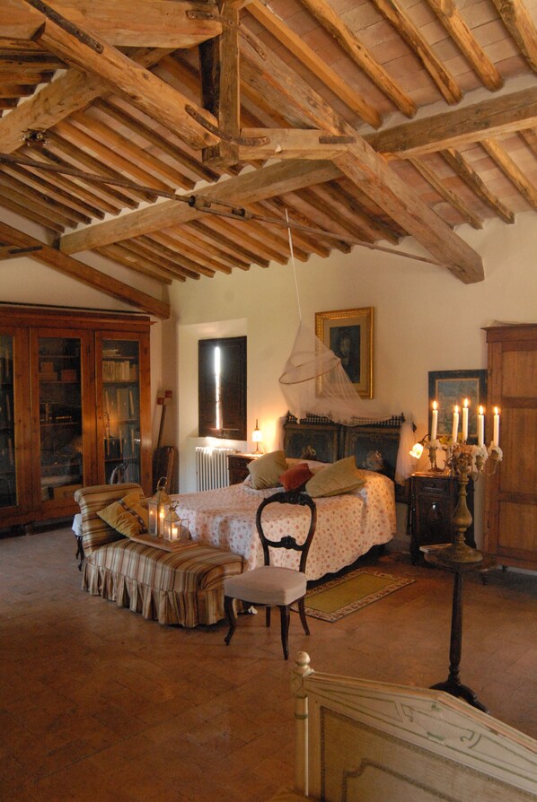 A rustic room with a bed, a chair, a table with candles, and a wooden ceiling. - Pieve di Caminino Historic Farm (Roccastrada)