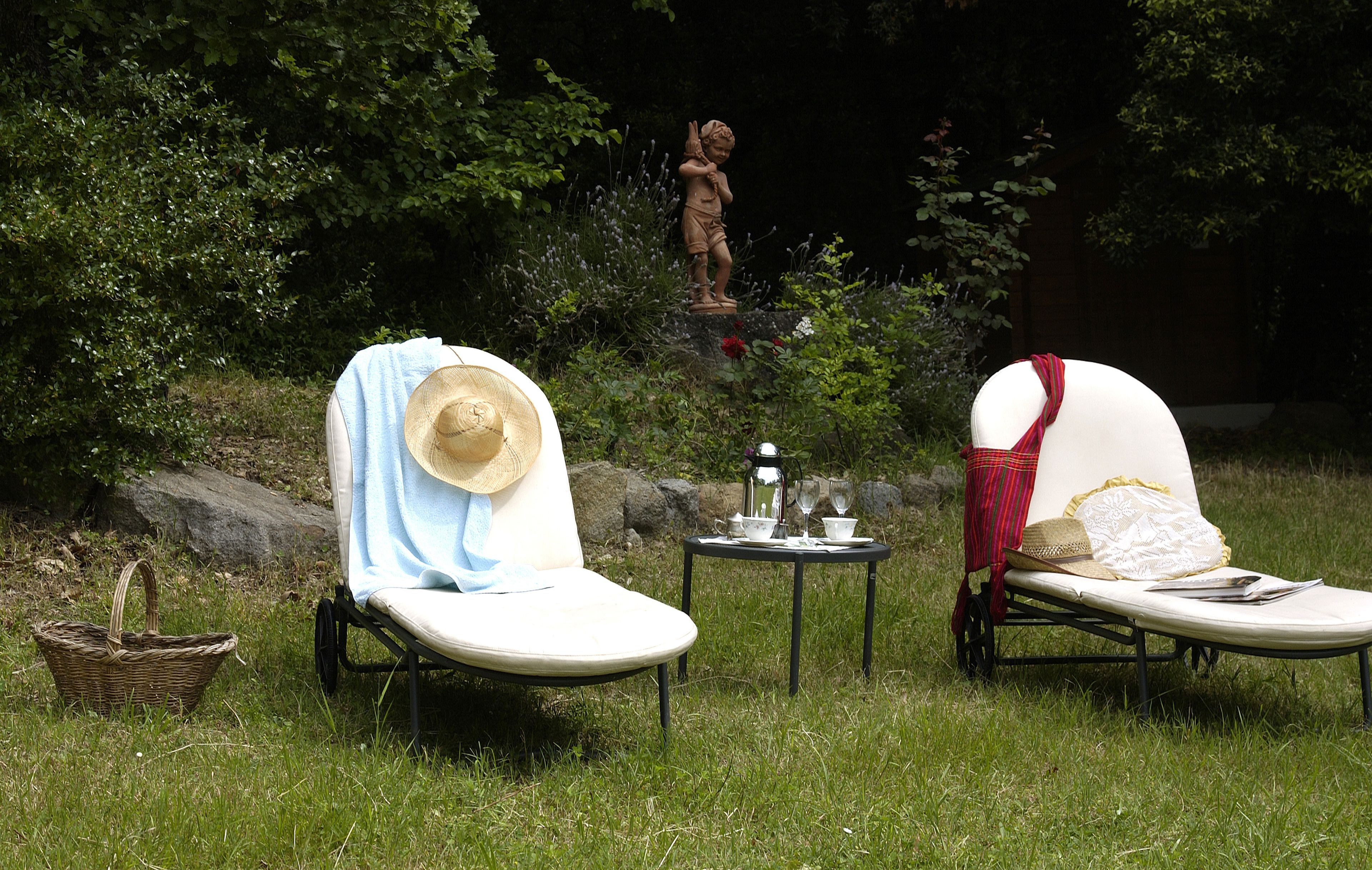 Two sun loungers with hats, a basket, and a statue in a grassy area with trees.