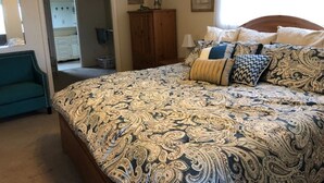 A bedroom with a large bed, a wooden wardrobe, a mirror, and a door leading to a bathroom. - FALL RATES ! Discounted rates. Book with Affirm. New Beach! (Dauphin Island)