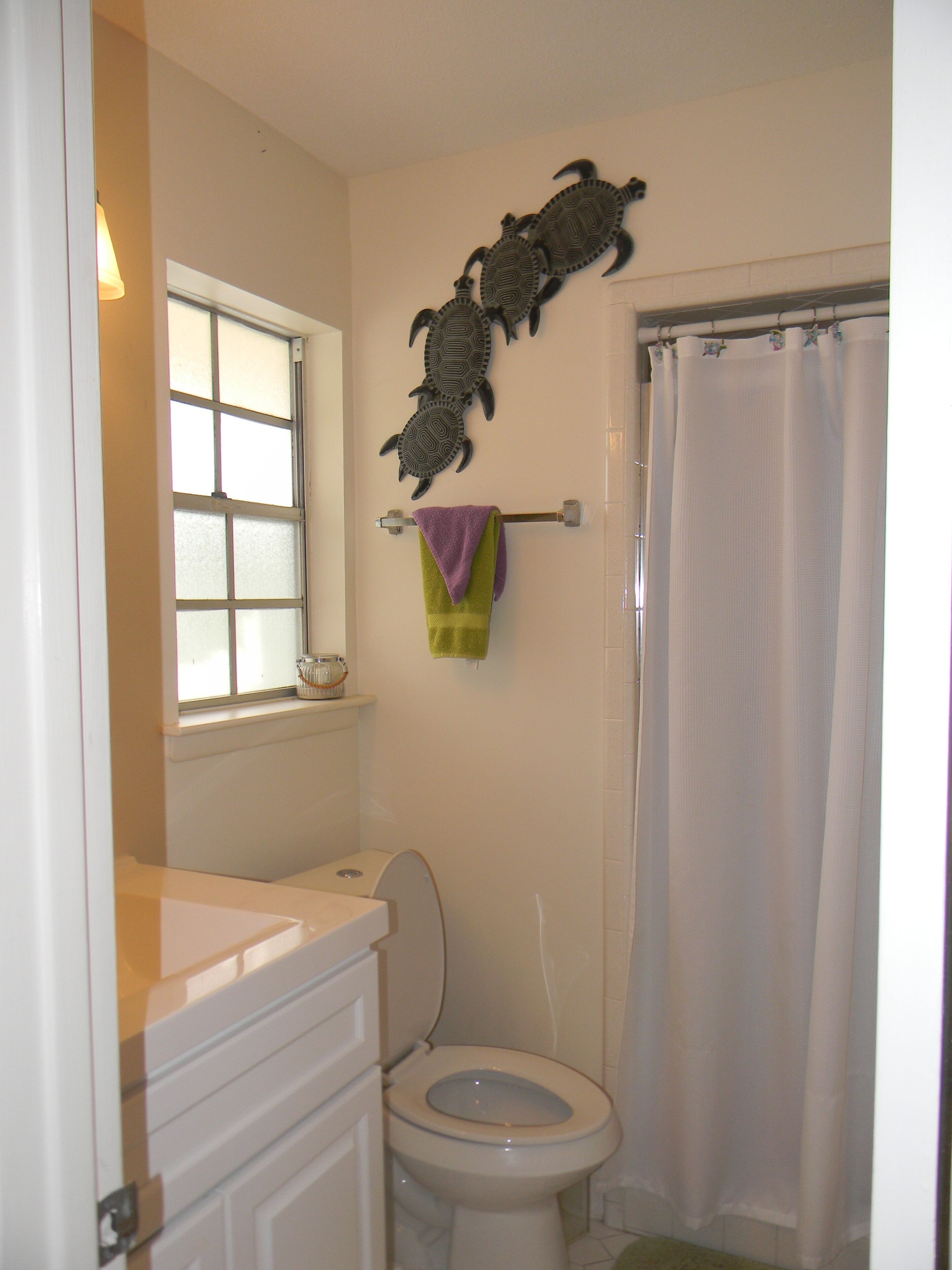Een badkamer met toilet, een raam, douchegordijn en een handdoekrek met handdoeken.