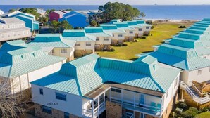 A row of modern buildings with blue roofs, a clear view of the ocean, and a well-maintained lawn. - FALL RATES ! Discounted rates. Book with Affirm. New Beach! (Dauphin Island)