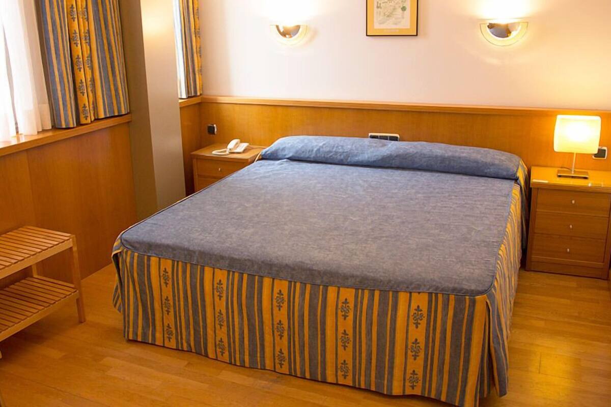 A hotel room with a bed, bedside tables, a chair, and a window with curtains.