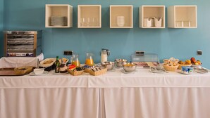 A breakfast buffet setup with various food items and utensils on a table against a blue wall. - Encasa Hotel Almansa (Almansa)