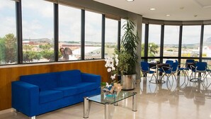 A modern waiting area with a blue sofa, a glass coffee table, and a large potted plant. - Encasa Hotel Almansa (Almansa)