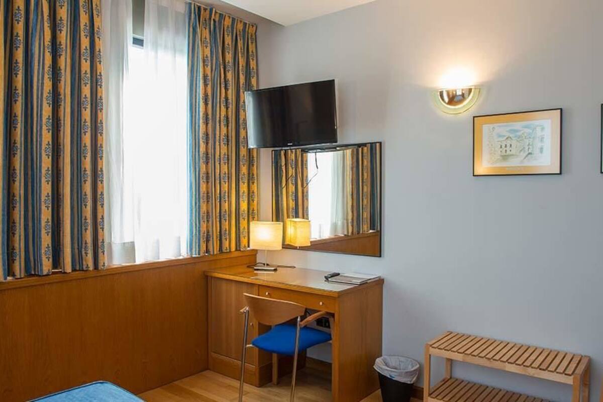 A hotel room with a desk, chair, television, and framed pictures on the wall.
