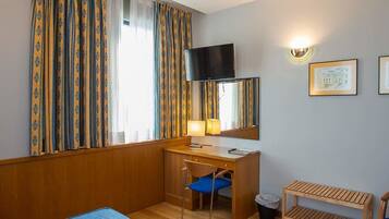 A hotel room with a desk, chair, television, and framed pictures on the wall.