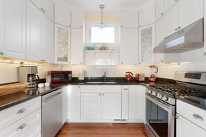 A modern kitchen with white cabinetry, a black countertop, stainless steel appliances, and a window above the sink.