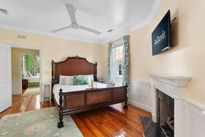 A bedroom with a wooden bed, a television mounted on the wall, and a fireplace.