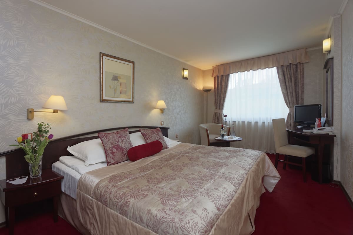 Quarto de hotel com uma cama grande, uma escrivaninha com computador, uma cadeira e uma pequena mesa.