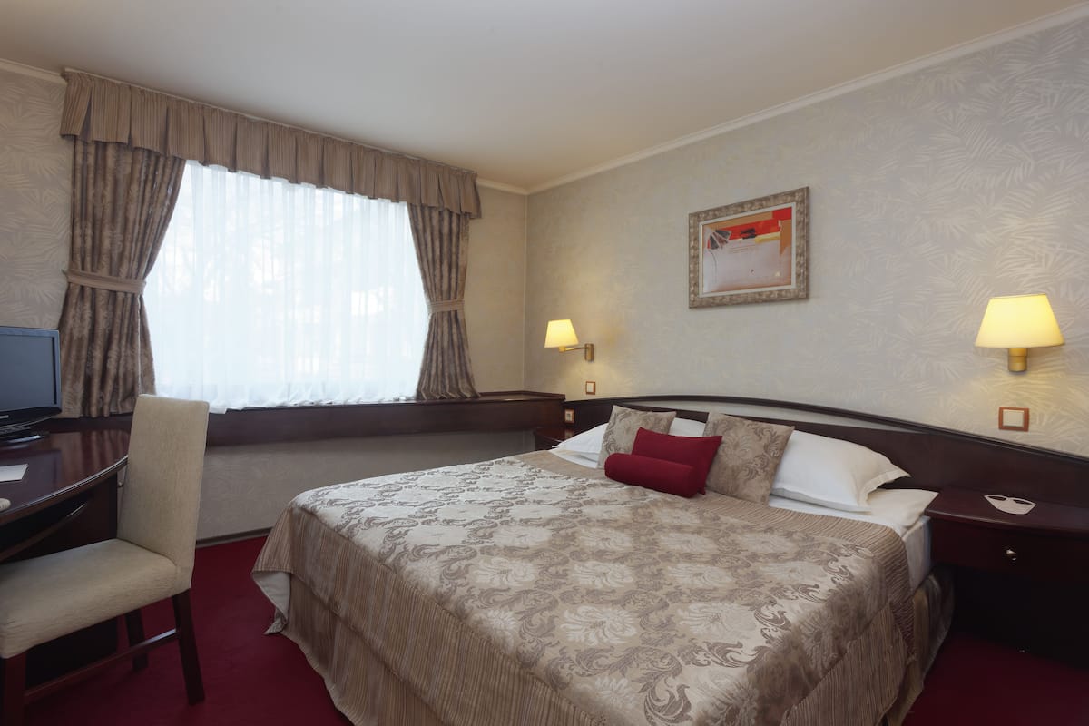 Quarto de hotel com cama, escrivaninha, cadeira, televisão e duas luminárias de cabeceira.