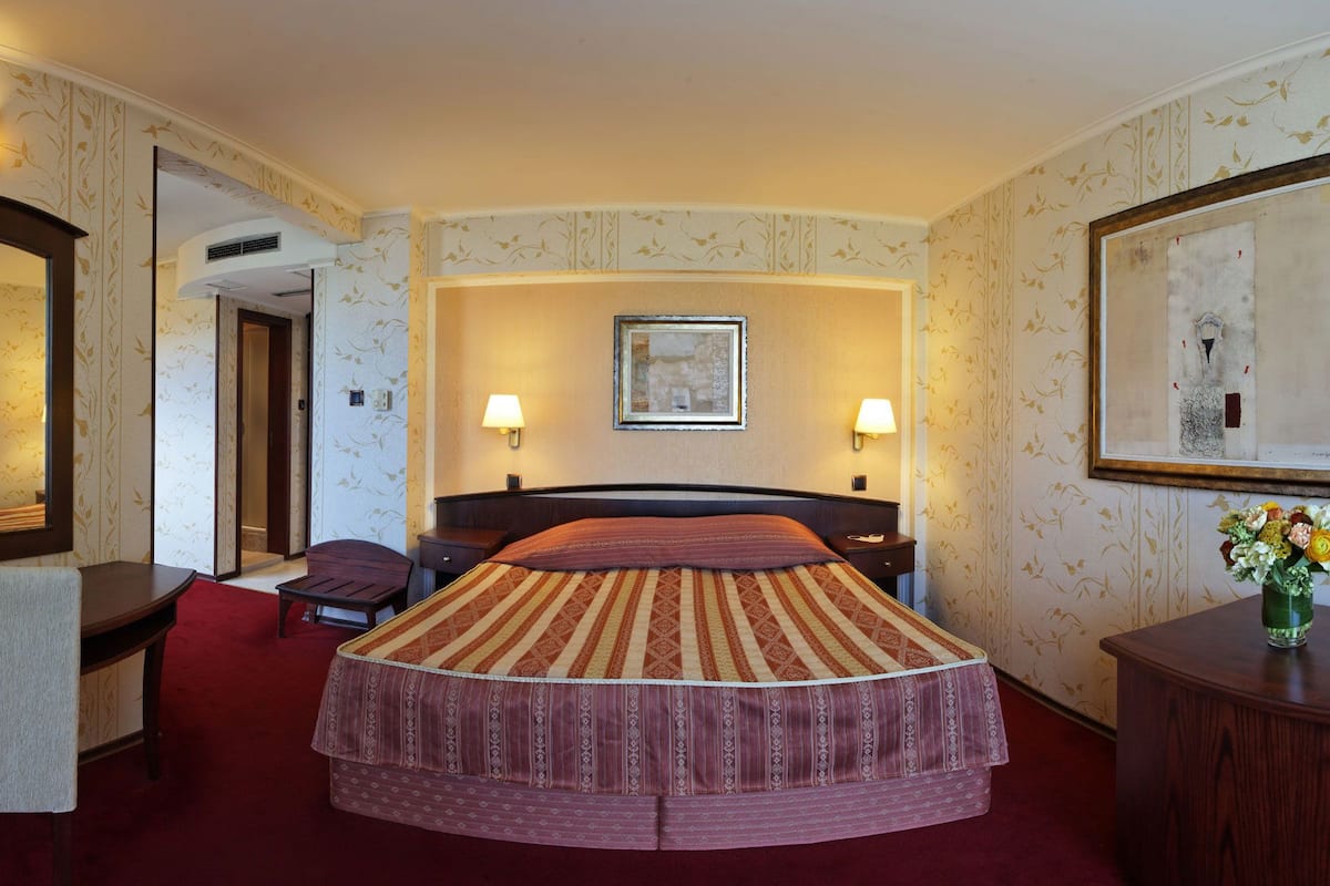 Quarto de hotel com uma cama grande, duas luminárias de cabeceira, um quadro na parede e um espelho sobre a cama.