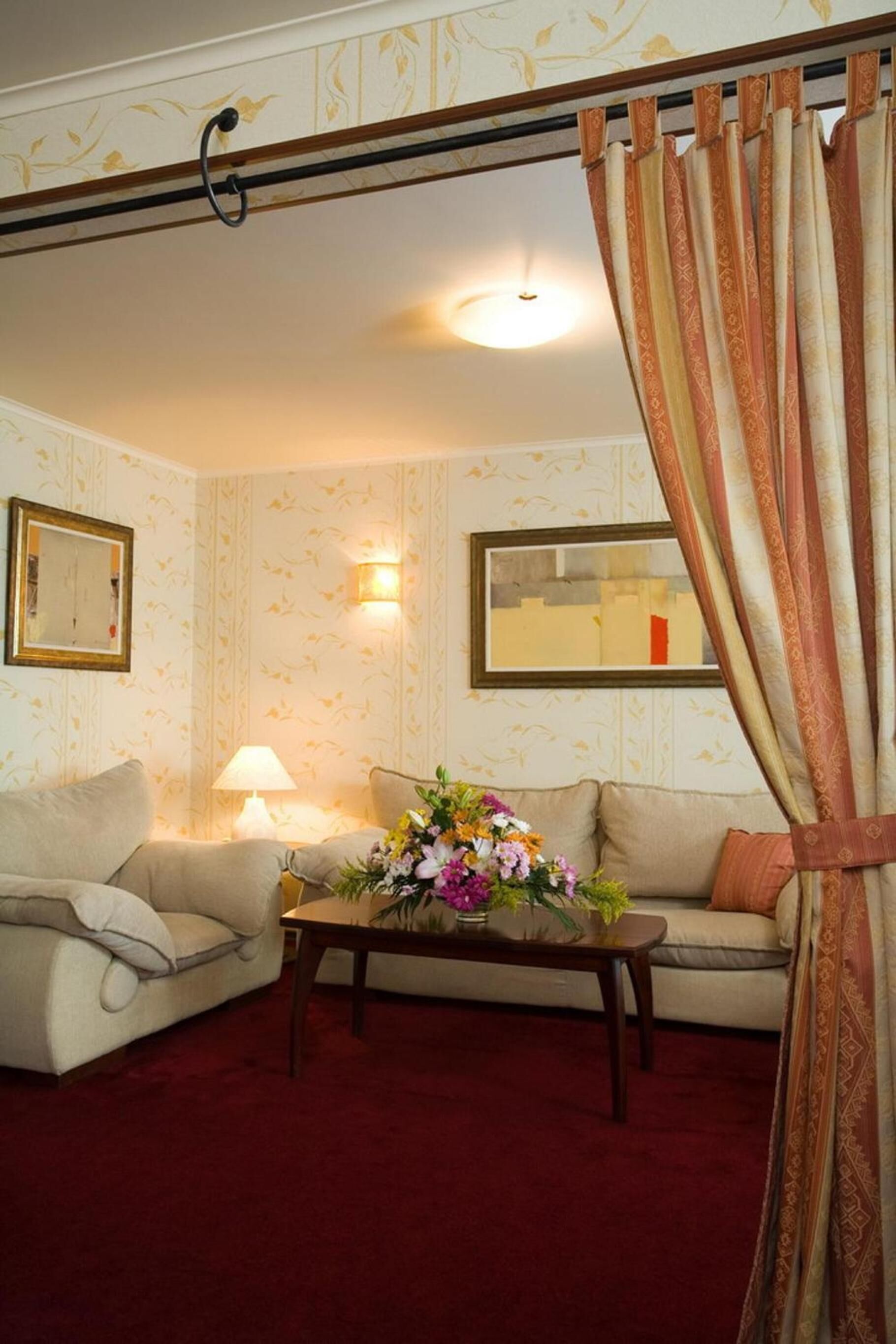A living room with a sofa, a table with a vase of flowers, a lamp, and a mirror on the wall.