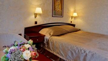 Quarto de hotel com uma cama, duas luminárias de cabeceira, um quadro na parede e uma mesa com um vaso de flores.
