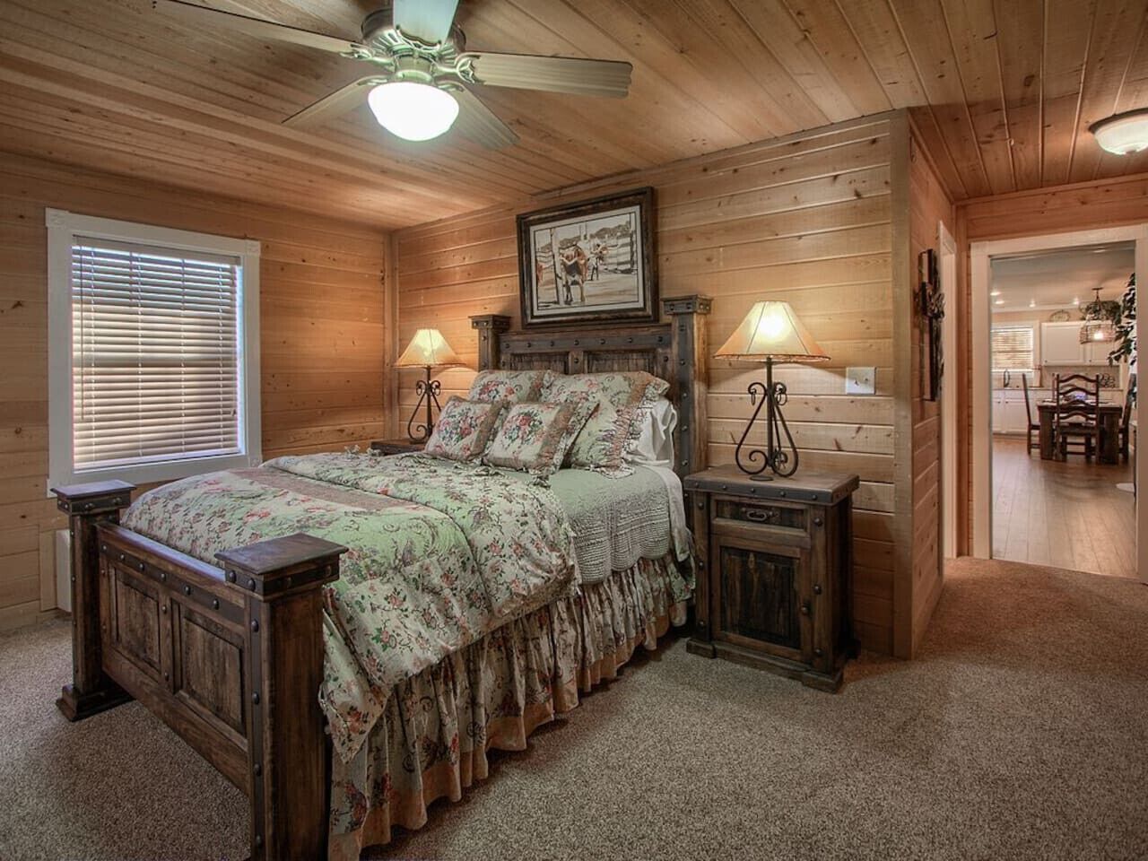 Une chambre dans une cabane en bois, avec un lit, deux tables de chevet, un ventilateur de plafond et un tableau encadré au mur.