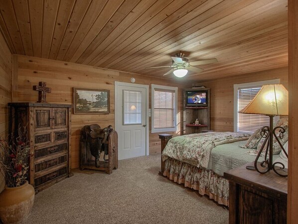 A cozy bedroom with a wooden ceiling, a bed with floral bedding, a television, and a lamp. - Lone Star Cabin No. 1 - Texas Hill Country (Fredericksburg)