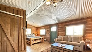 A log cabin interior with a bed, sofa, and coffee table. - 32 MI to YNP | Pet Friendly | Sleeps 2 (Island Park)