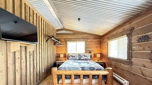 A wooden cabin bedroom with a bed, a window, and a ceiling fan. - 32 MI to YNP | Pet Friendly | Sleeps 2 (Island Park)