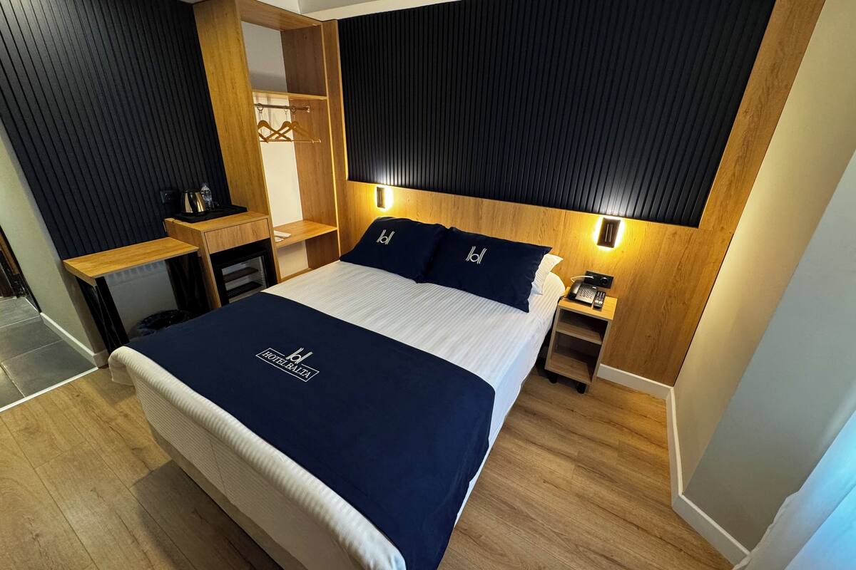 Habitación de hotel con una cama grande, un escritorio de madera, un armario y una mesita de noche con teléfono.