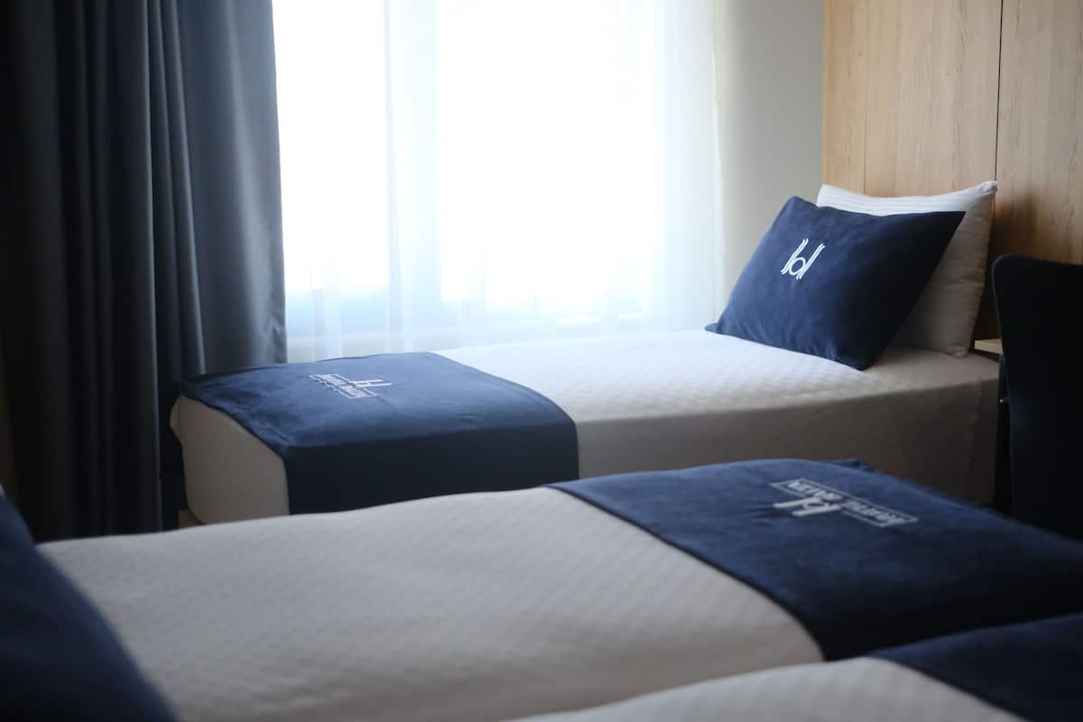 Habitación de hotel con dos camas, cada una con una colcha azul oscuro y almohada a juego.