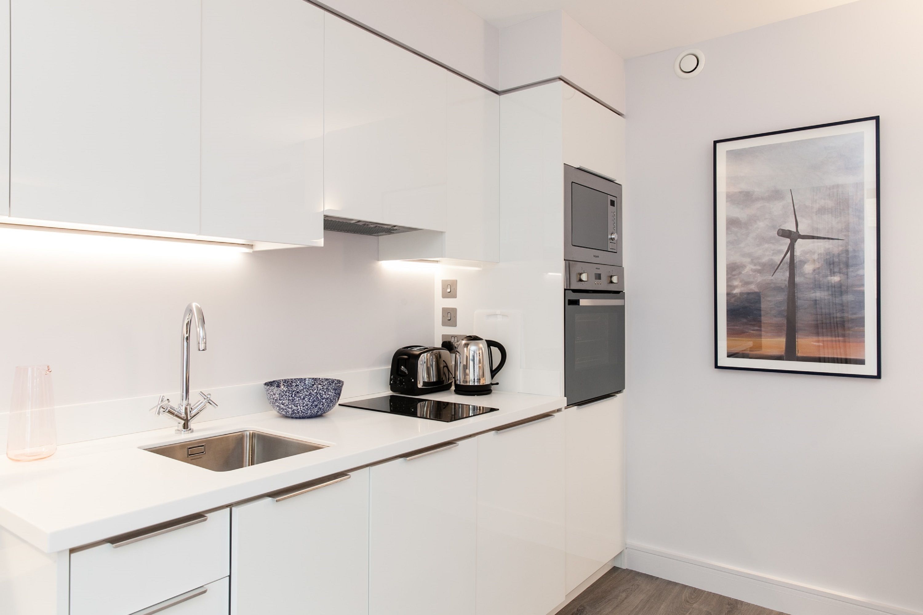 A modern kitchen with white cabinets, stainless steel appliances, and a framed picture of wind turbines on the wall.