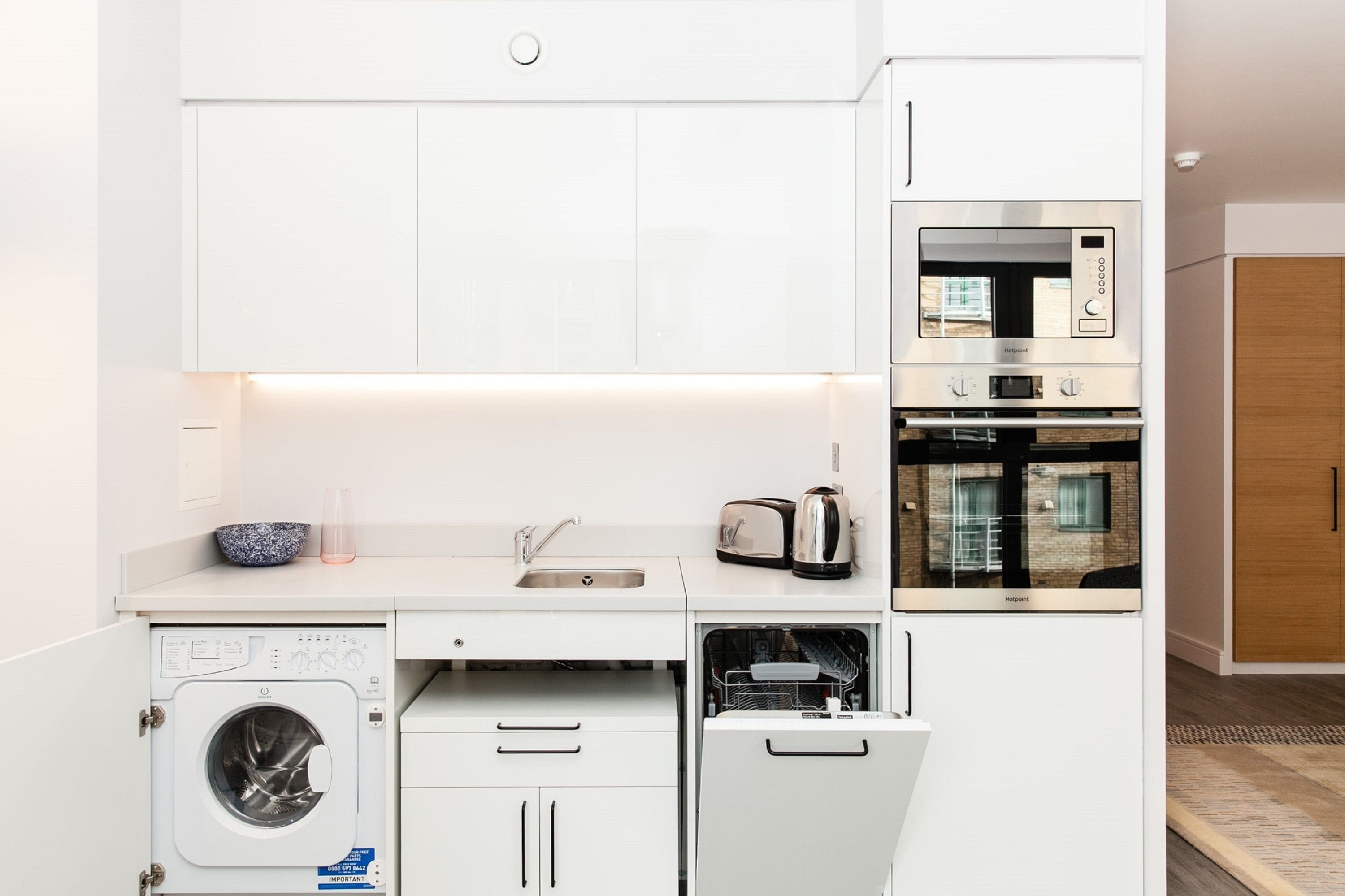 Een kleine keuken met een wasmachine, vaatwasser, magnetron en broodrooster.