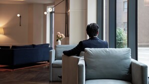 A modern hotel lobby with a seating area, a large window, and a vase with flowers.