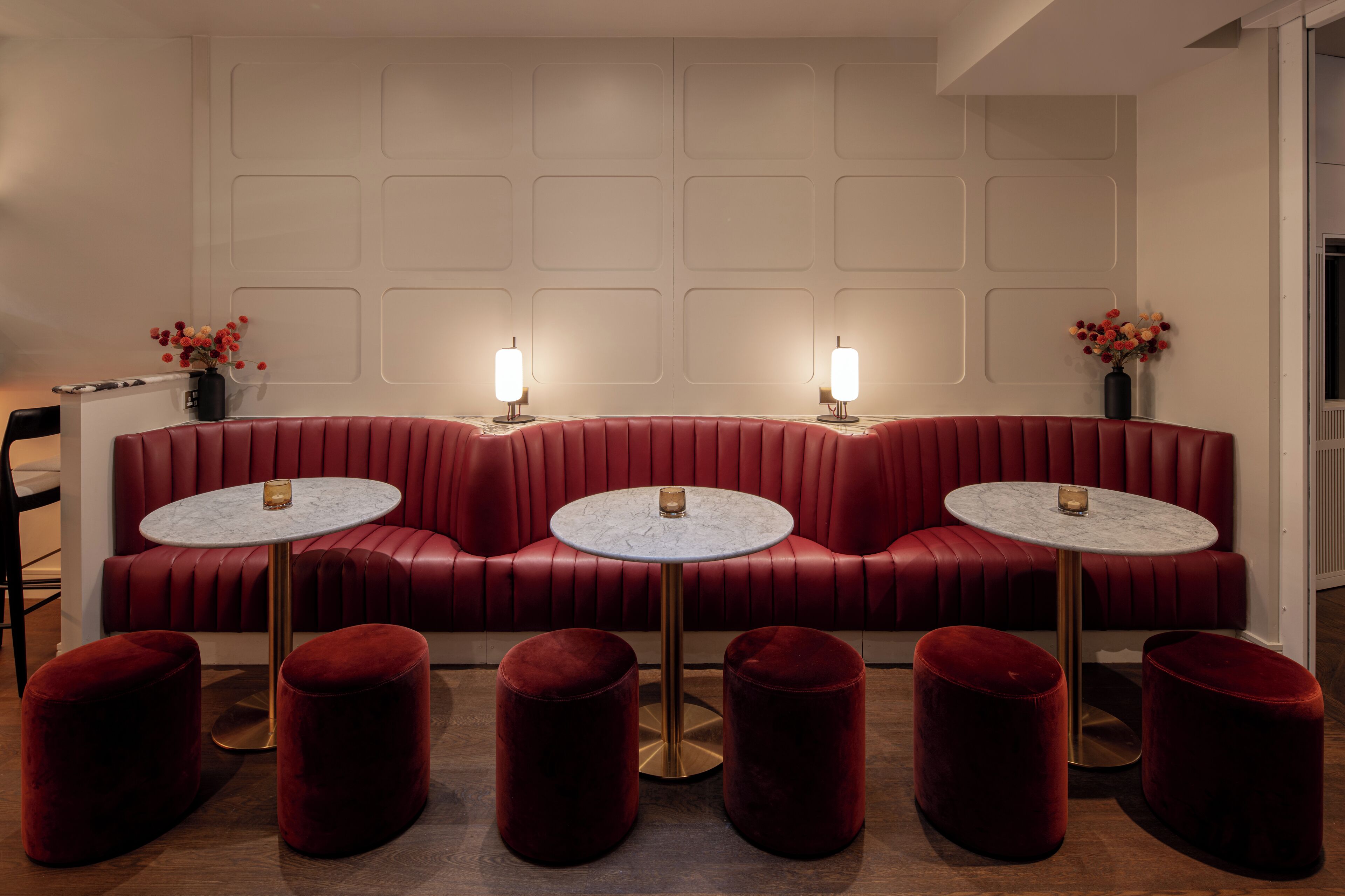 Un canapé en cuir rouge, devant lequel se trouvent trois petites tables rondes, chacune portant une bougie.