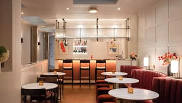 Een modern restaurantinterieur met ronde tafels, rode, beklede zitbanken en een bar met wijnrek.