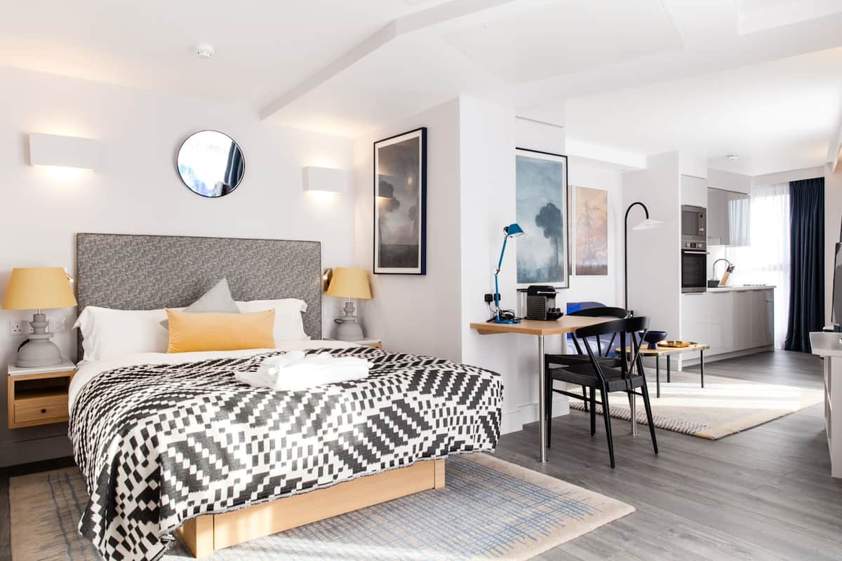 A modern hotel room with a large bed, a desk, and a kitchenette.