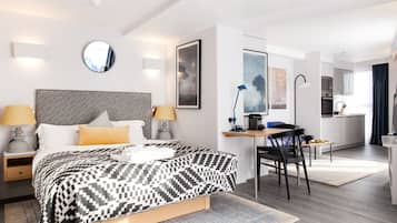 A modern hotel room with a large bed, a desk, and a kitchenette.