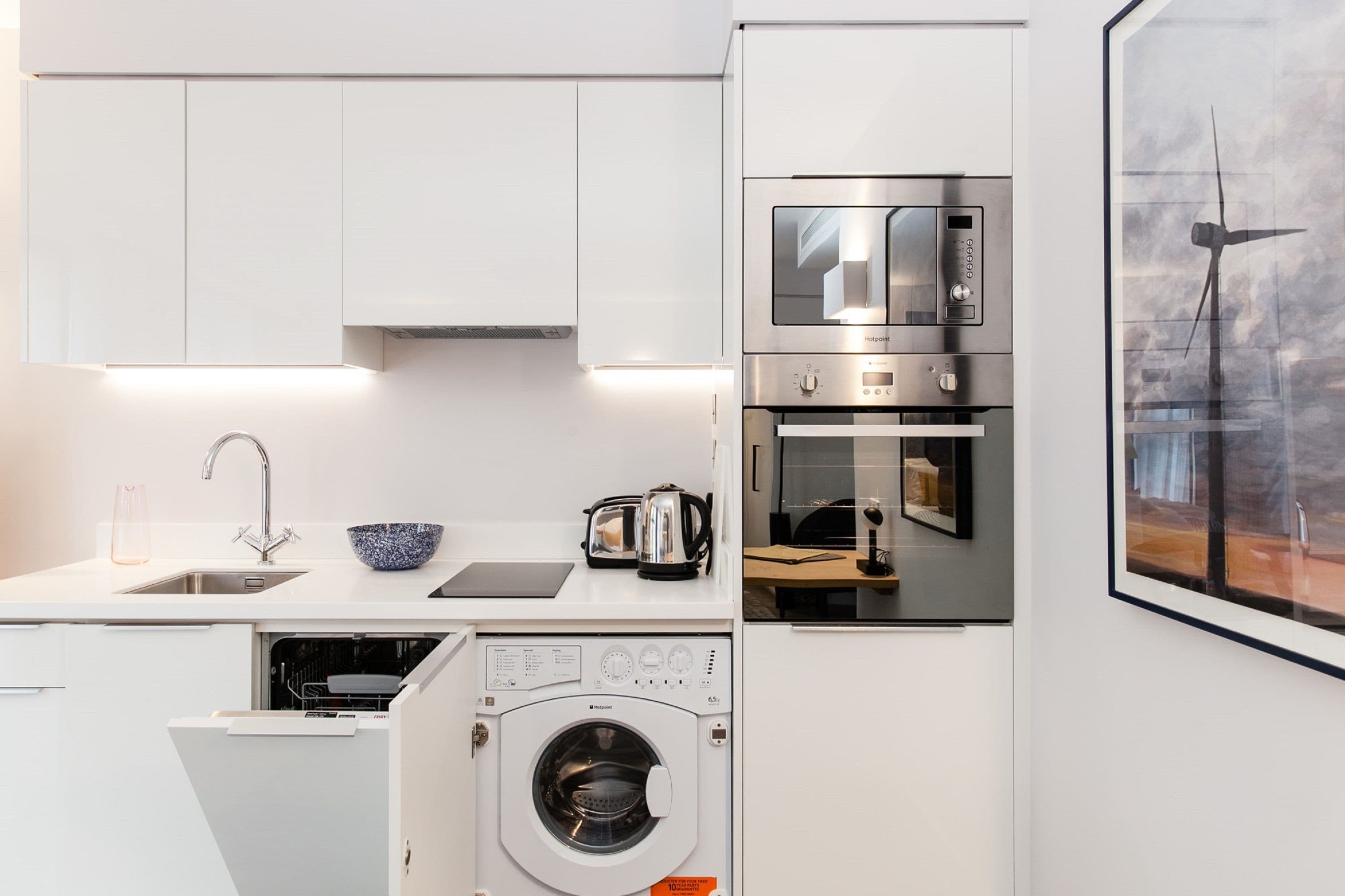 Een kleine keuken met witte kastjes, een inbouwvaatwasser, een voorlader wasmachine, een magnetron en een broodrooster.