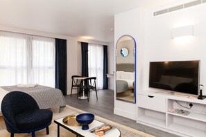 A modern hotel room with a bed, a desk, a chair, a TV, and a mirror. - Rockwell East (London)