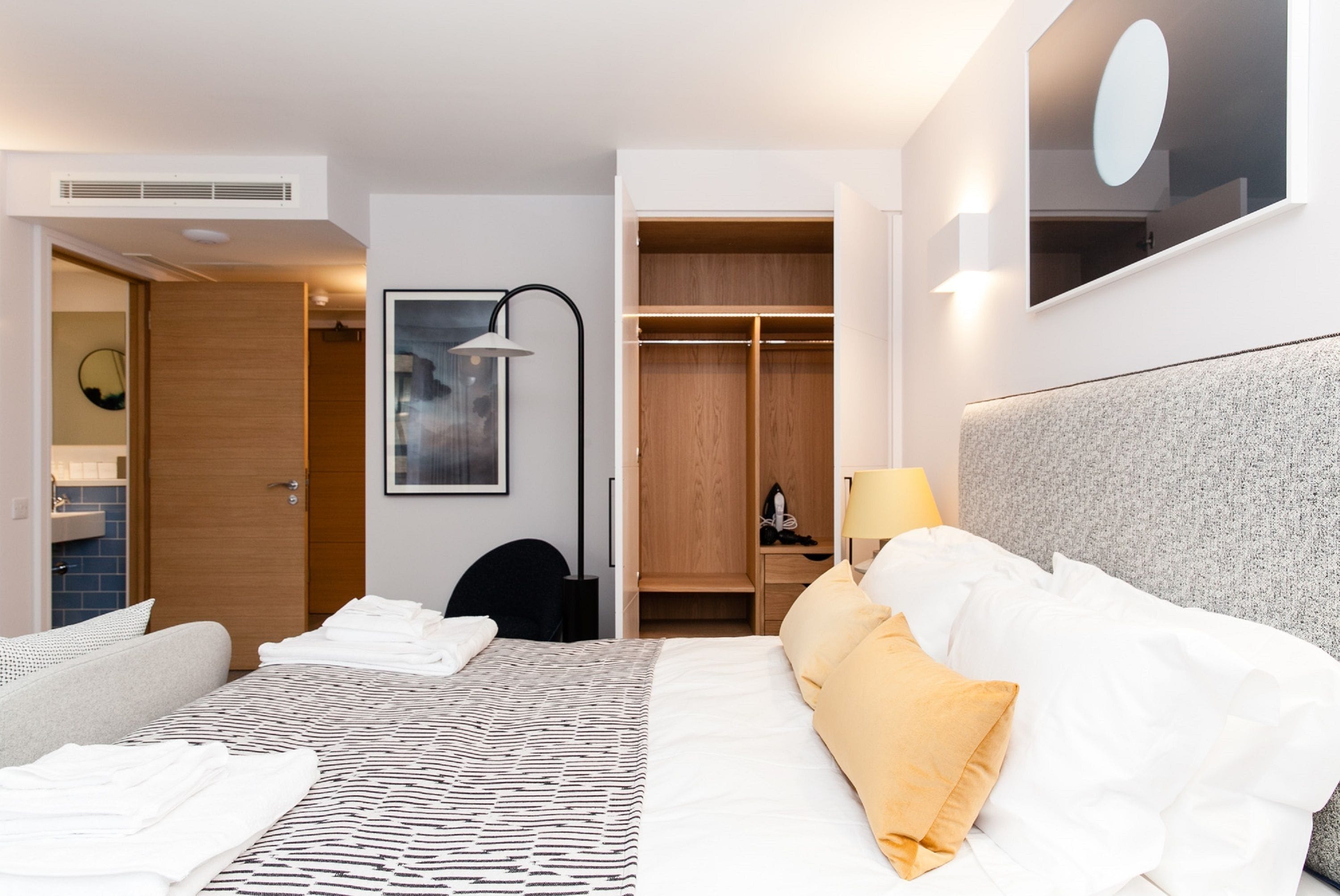 Une chambre d’hôtel comprenant un lit, une table de chevet, une lampe et un dressing.