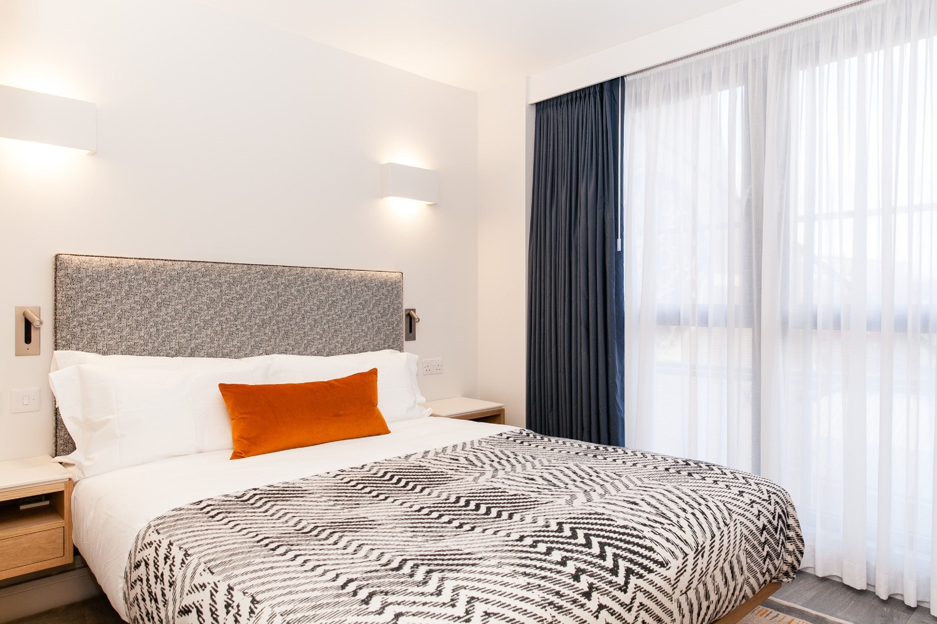 A hotel room with a bed, a nightstand, and a wall-mounted lamp.