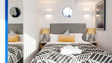 Une chambre d’hôtel avec un grand lit, deux tables de chevet avec des lampes, un miroir rond et un tableau encadré au mur.