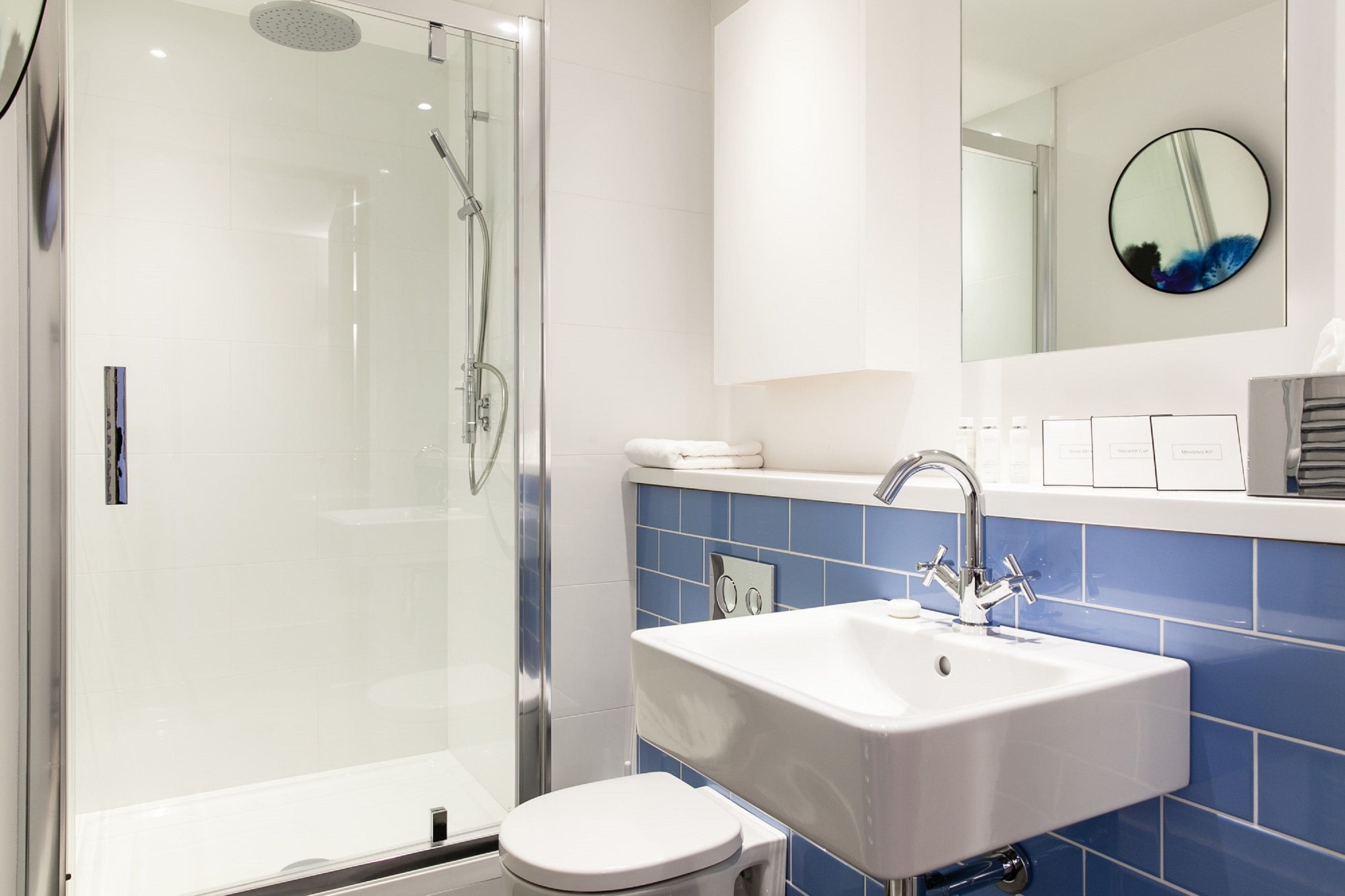 Ein modernes Badezimmer mit einer einteiligen Glasdusche, einem weißen Waschbecken und einem großen Spiegel.