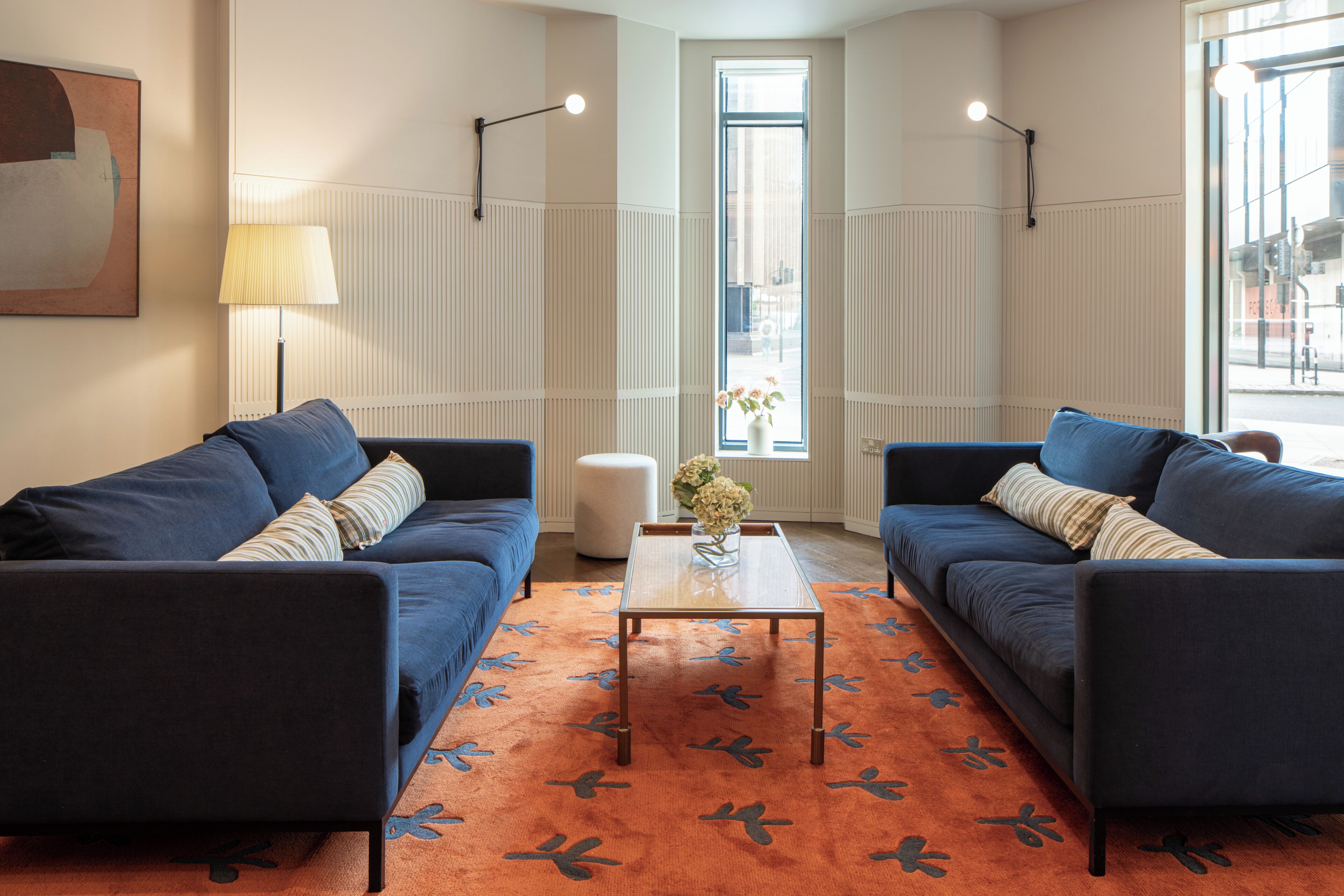 A modern living room with two dark blue sofas, a glass coffee table, and a patterned orange rug.
