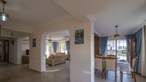 A spacious living area with a dining table and chairs, a sofa, and a large window with curtains. - Infinity Civan Villa (Fethiye)